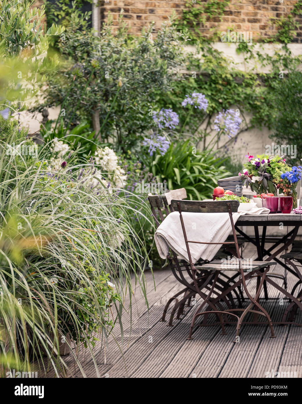 Vecchio bistrò francese sedie intorno a lungo tavolo in legno su giardino terrazza sul tetto con impalcati. Agapanthus e gelsomino fiorisce in background Foto Stock