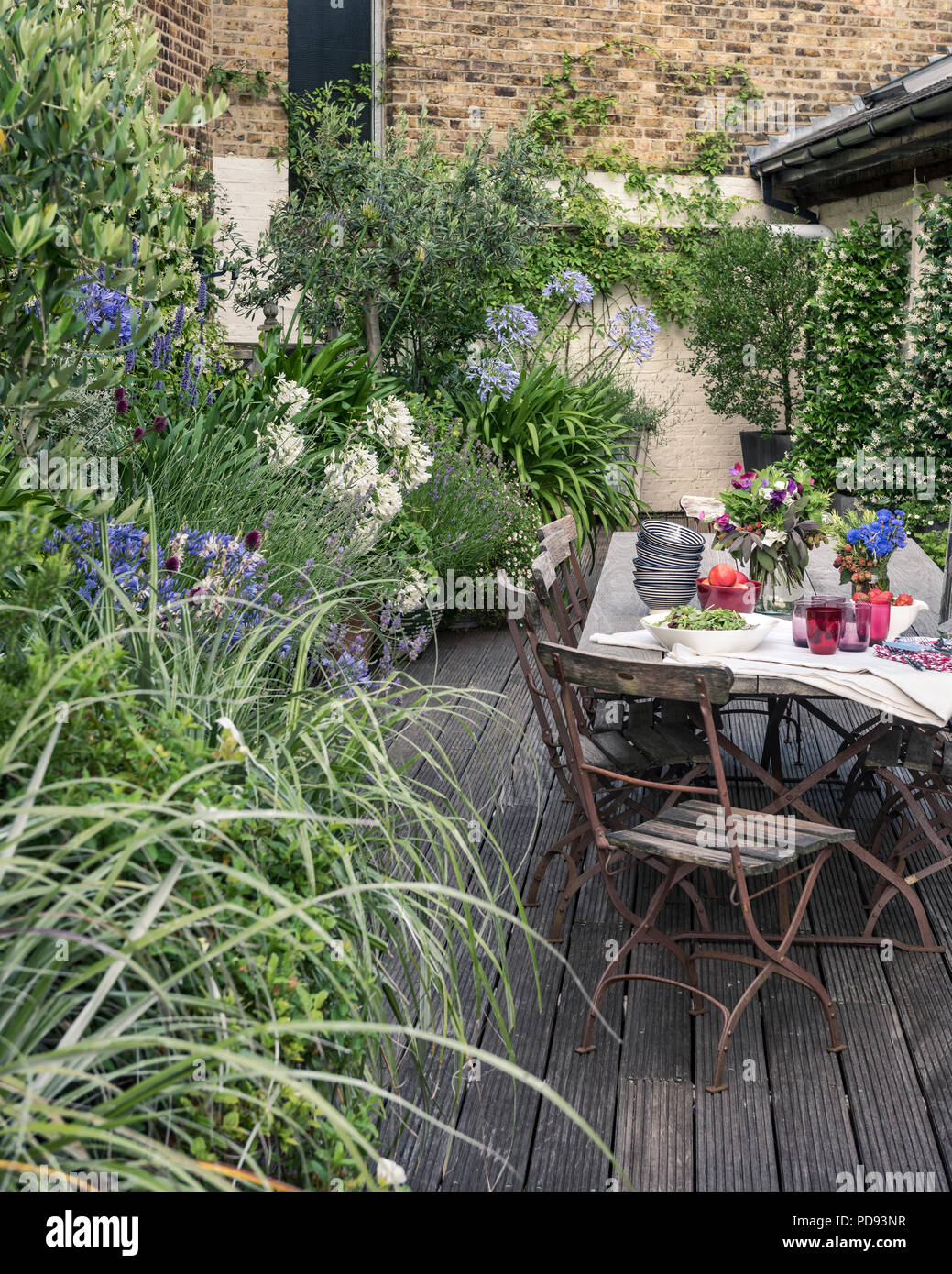 Vecchio bistrò francese sedie intorno a lungo tavolo in legno su giardino terrazza sul tetto con impalcati. Agapanthus e gelsomino fiorisce in background Foto Stock