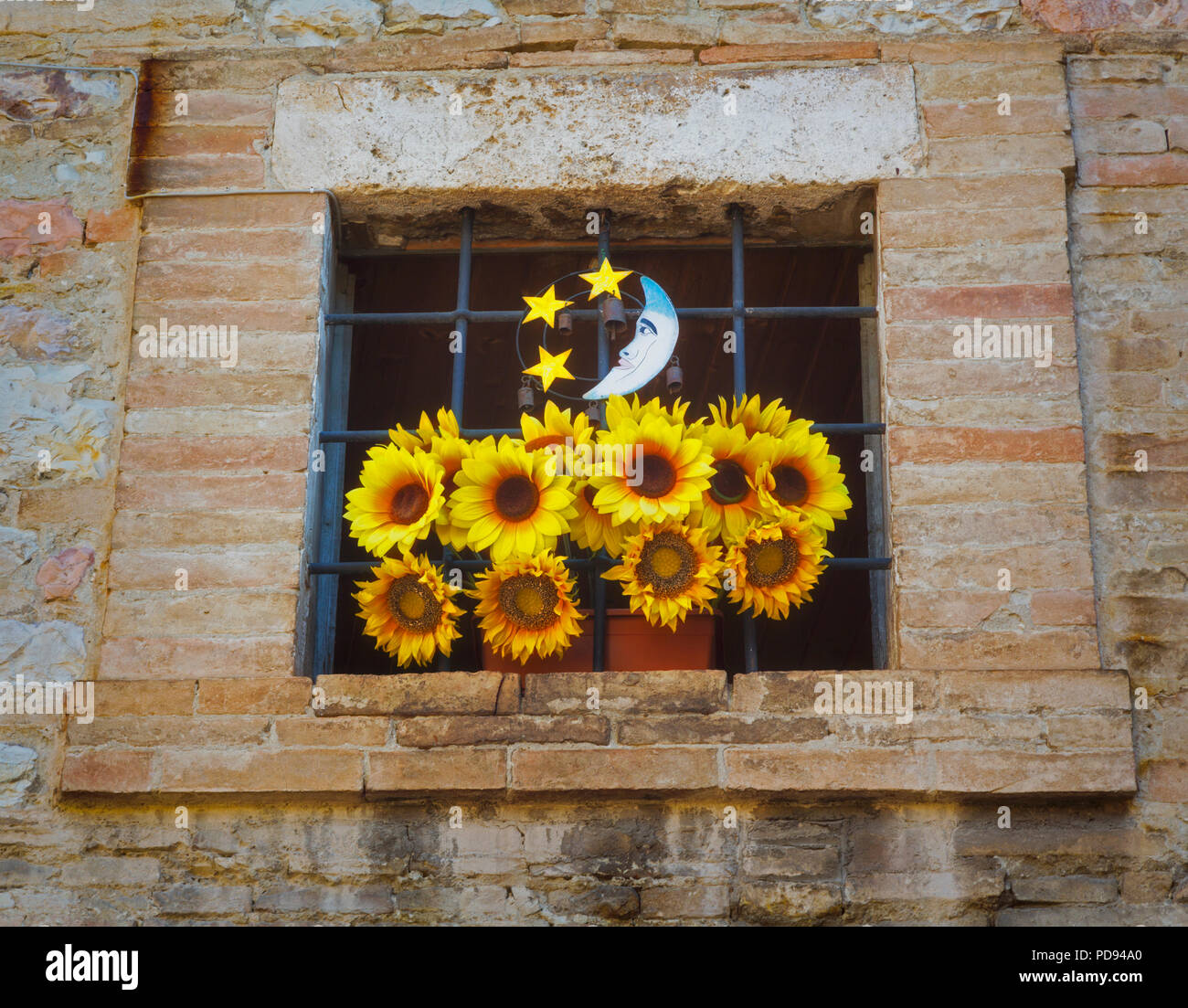 Assisi, la provincia di Perugia, Umbria, Italia. Una antica finestra sbarrata decorate con girasoli e un piccolo impianto che rappresenta la luna e le stelle. Foto Stock