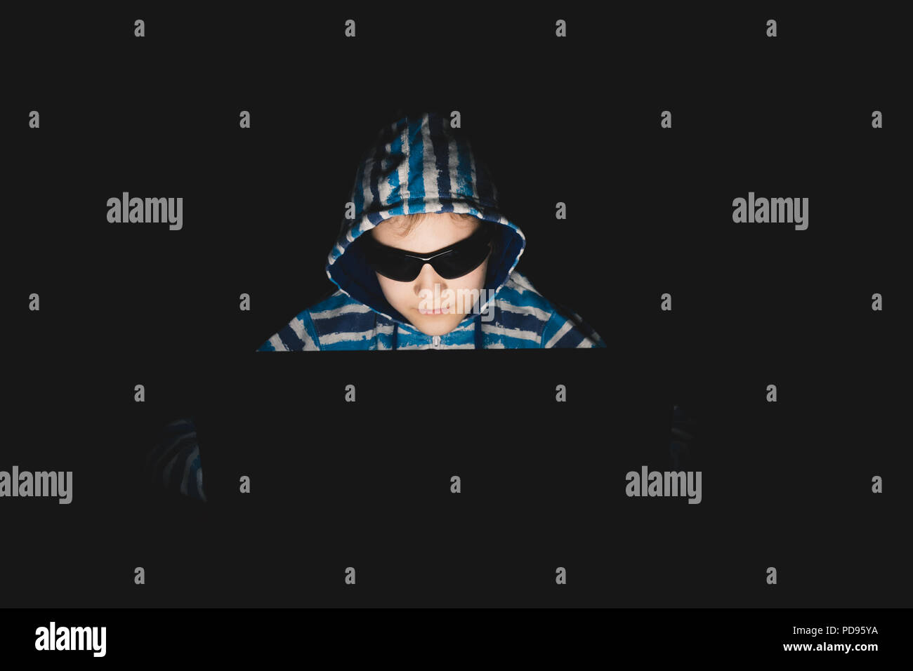 Ragazza hacker in una felpa con cappuccio utilizzando computer portatile in una stanza buia. Con gli occhiali da sole. Foto Stock