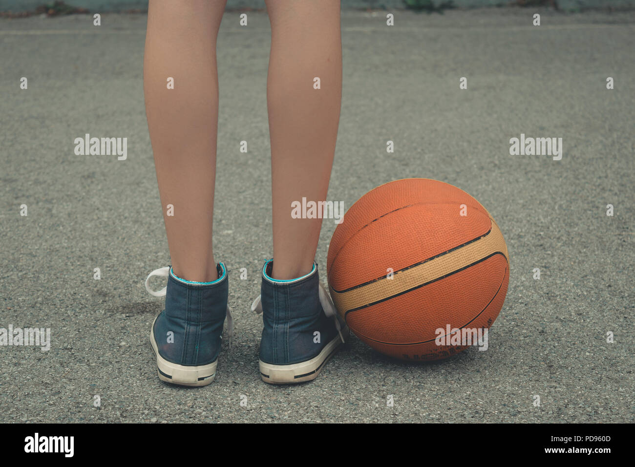 Giovane ragazza gambe indossando sneakers in piedi accanto alla sfera sul campo da pallacanestro con superficie in calcestruzzo. Basso angolo vista ravvicinata. Foto Stock