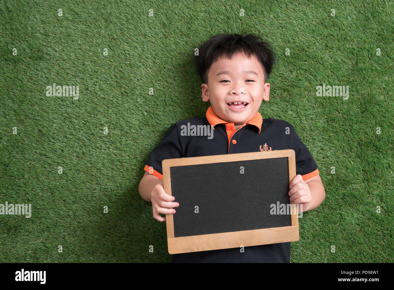 Carino asian bambino giacente e tenendo la lavagna su erba verde Foto Stock