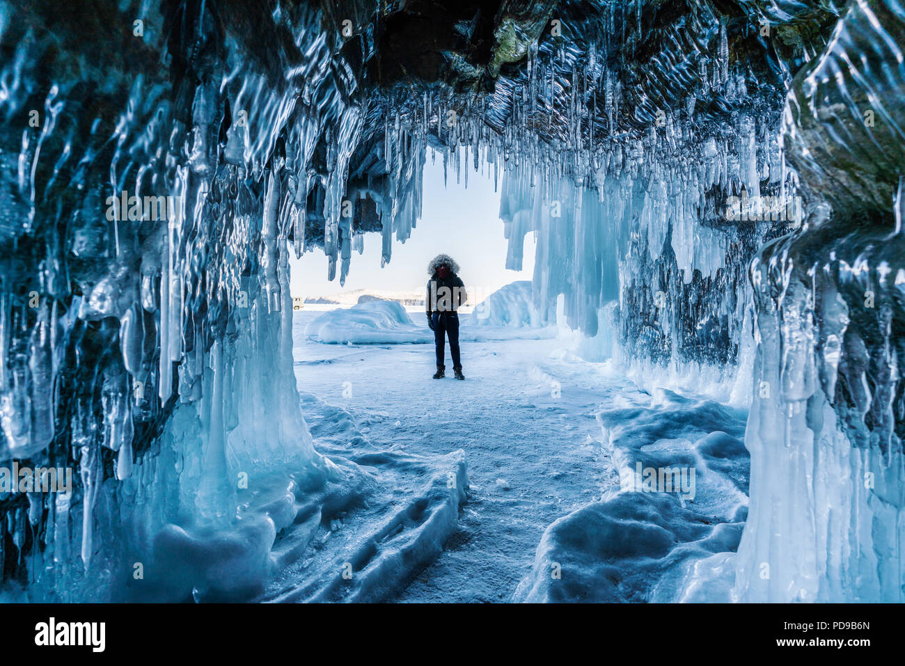 Viaggiare in inverno, un uomo in piedi sul lago ghiacciato Baikal con la grotta di ghiaccio di Irkutsk in Siberia, Russia Foto Stock