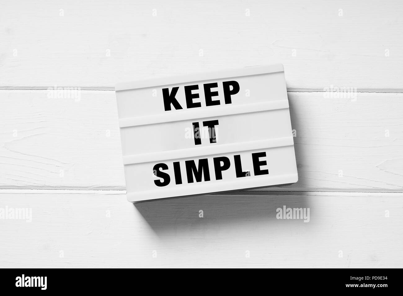 Keep it simple text su lightbox segno, minimo lay piatto design bianco su sfondo di legno, semplicità o concetto minimalista Foto Stock
