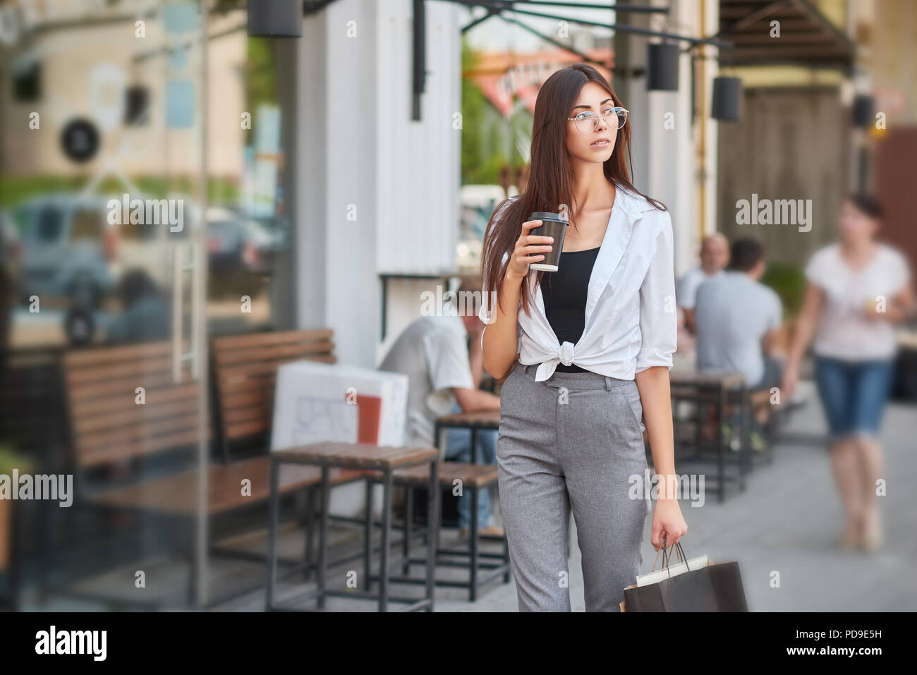 Elegante studente a piedi nel centro cittadino di bere caffè, portando i  sacchi di carta dal negozio, indossando di moda classica grigia pantaloni e  camicia bianca, guardando Foto stock - Alamy