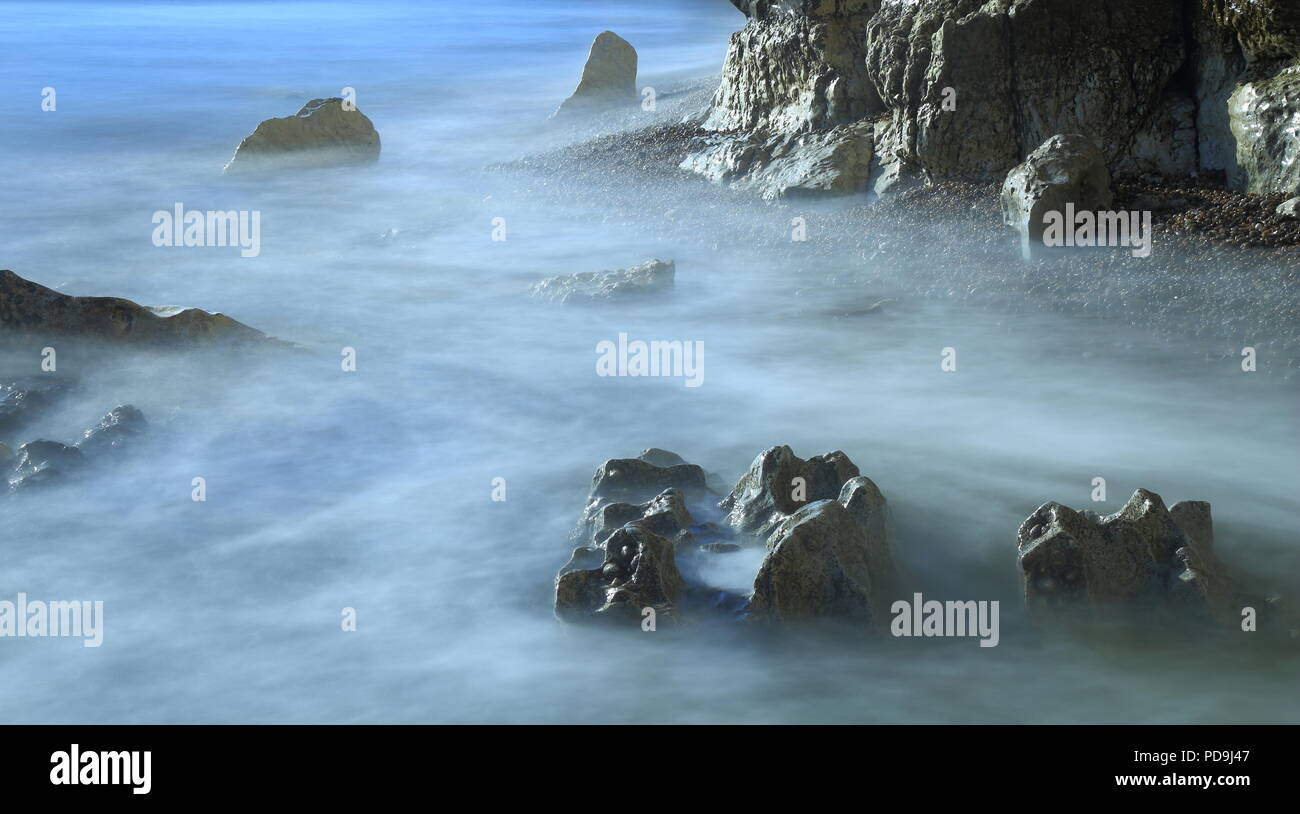 Sfocata onde del mare su una spiaggia rocciosa in East Devon su Jurassic Coast Foto Stock