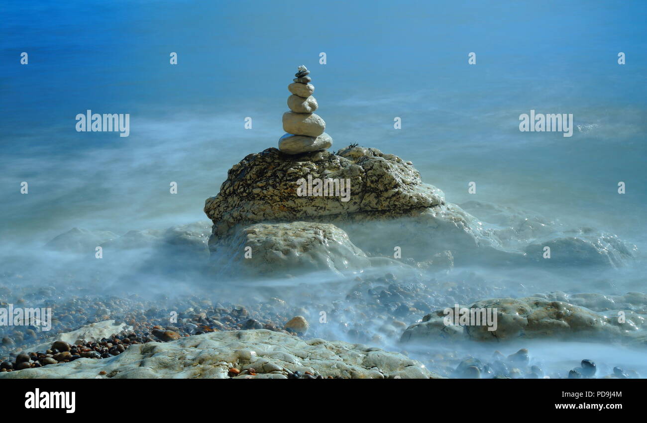Pila di pietre di bilanciamento sulla spiaggia di ciottoli circondata da sfocata onde del mare Foto Stock