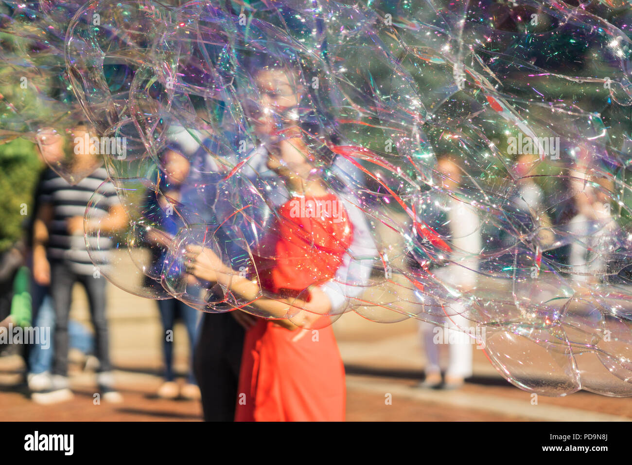 Giovane a giocare con il gigante arcobaleno bolle di sapone galleggianti in estate aria durante una bella giornata di sole. Divertente gioco divertente per i bambini e gli adulti. Foto Stock