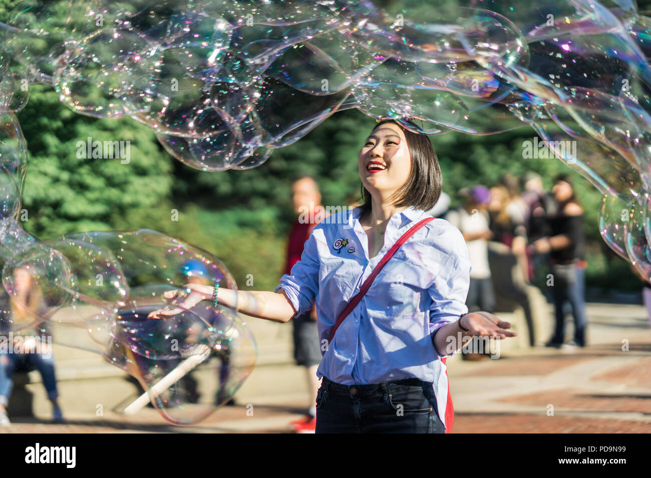 La città di New York, Stati Uniti - il 24 settembre 2016. Giovane donna a giocare con il gigante arcobaleno bolle di sapone galleggianti in aria di estate Foto Stock