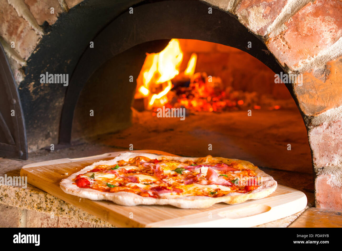 Rustico pizza fatta in casa il prosciutto cotto in forno a legna per la  stufa in mattoni con fuoco in background Foto stock - Alamy