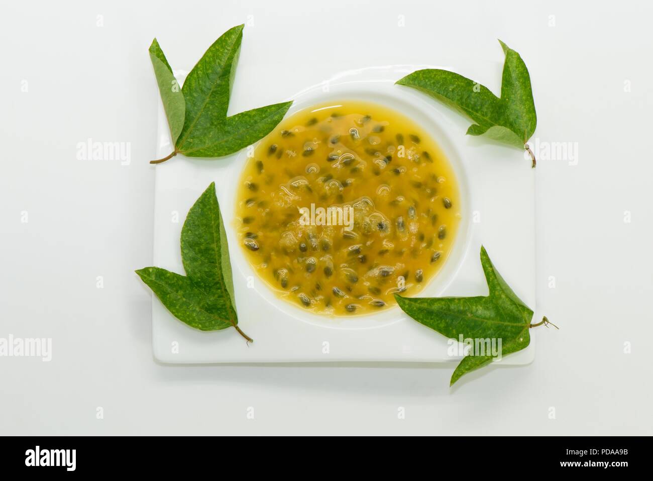 Succo di frutto della passione con foglie verdi sulla piastra bianca Foto Stock