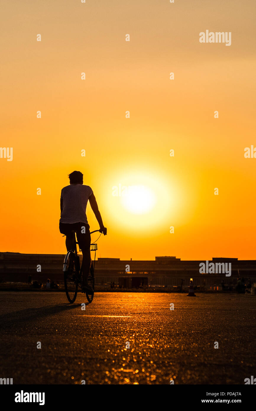 Silhouette di una persona in Bicicletta Equitazione con il tramonto sullo sfondo del cielo Foto Stock