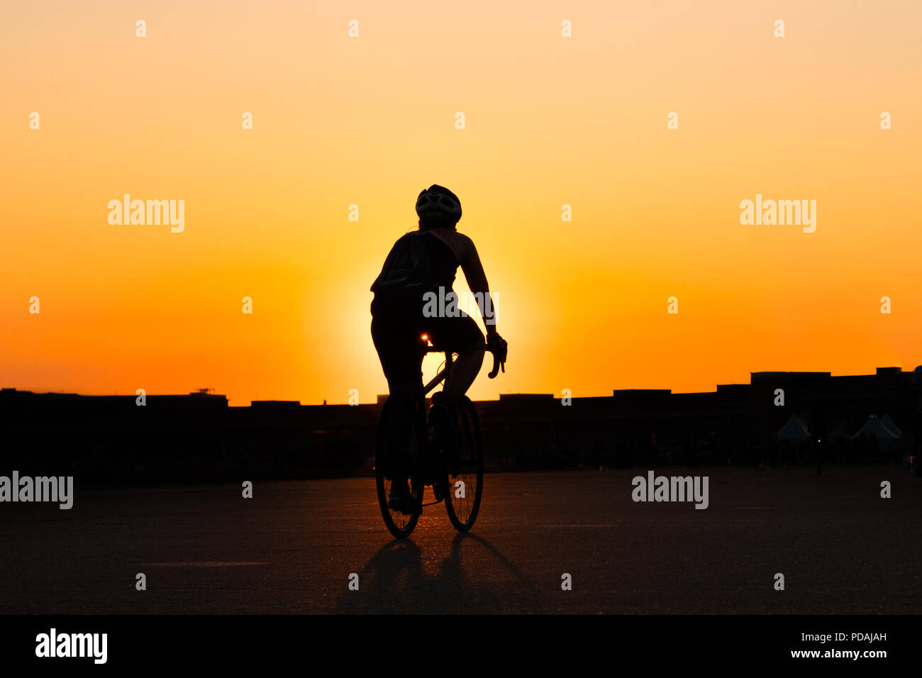 Silhouette di una persona in Bicicletta Equitazione con il tramonto sullo sfondo del cielo Foto Stock