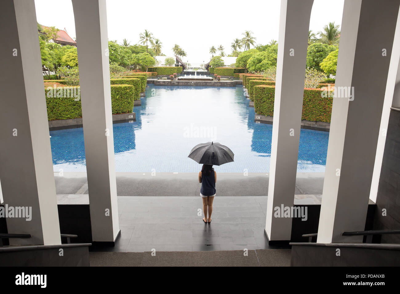 Donna con ombrello in piedi da piscina guardando la pioggia in vacanza. Foto Stock