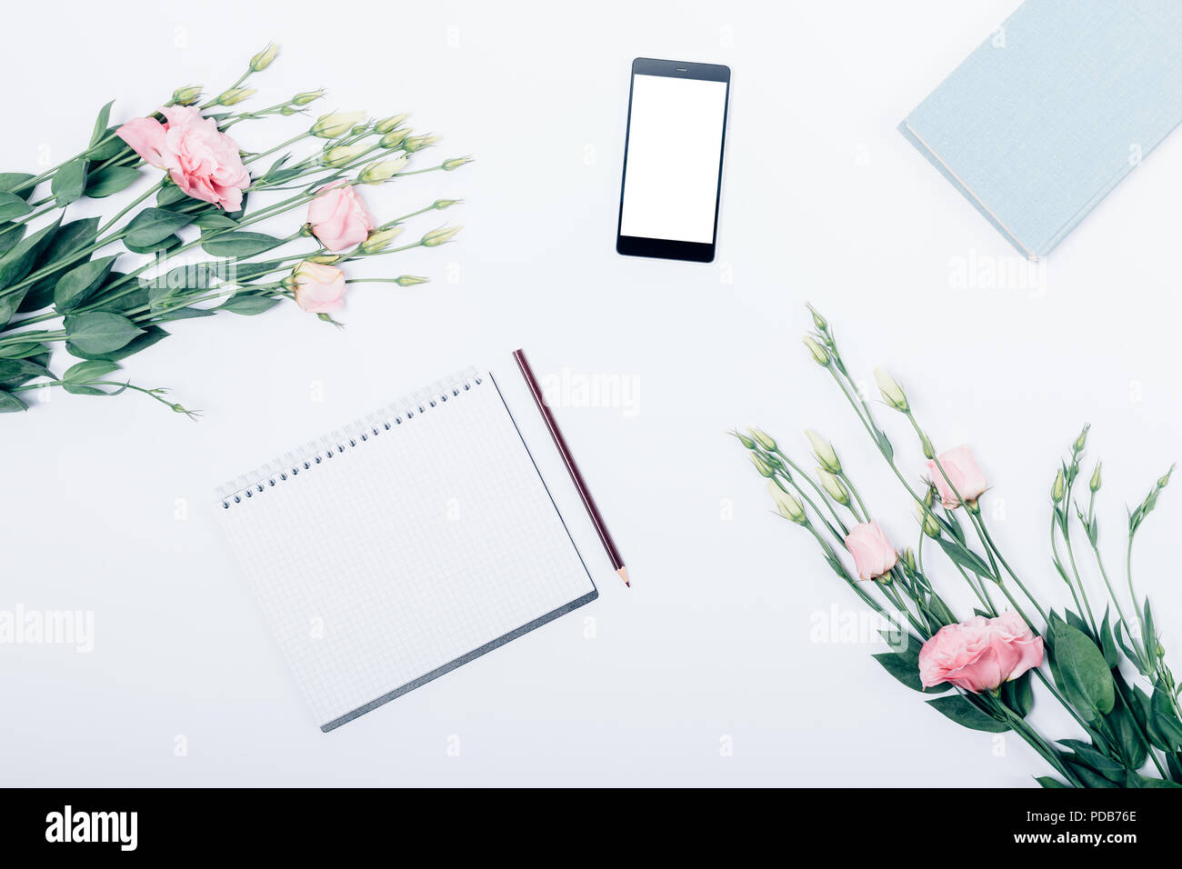 Vuoto il blocco note con matita vicino a libro, telefono cellulare e bouquet di fiori, vista dall'alto. Piano di composizione laico femminile stilizzata sul posto di lavoro. Foto Stock