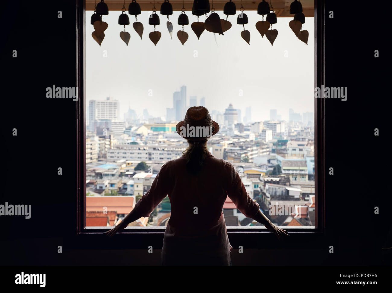 Silhouette di donna turistica cercando nella finestra per Bangkok City View grattacieli del quartiere degli affari da Golden Mountain Pagoda Wat Saket al coperto Foto Stock