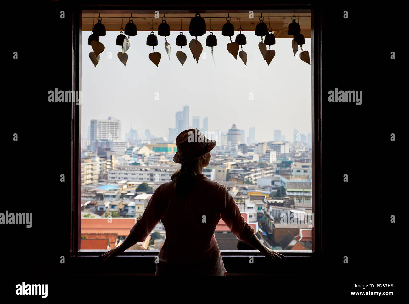 Silhouette di donna turistica cercando nella finestra per Bangkok City View grattacieli del quartiere degli affari da Golden Mountain Pagoda Wat Saket al coperto Foto Stock
