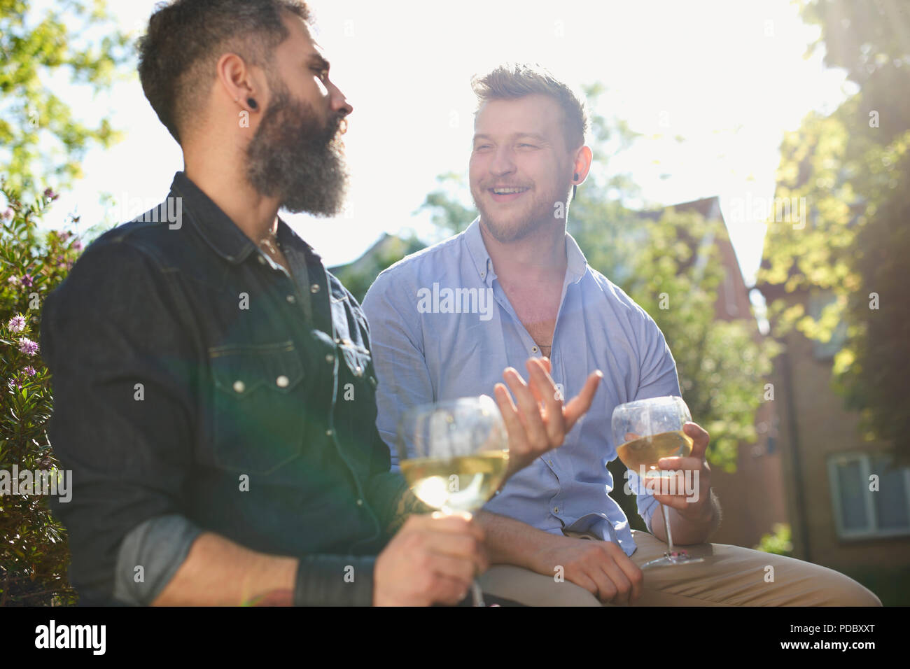 Maschio sorridente coppia gay di bere vino bianco nel giardino soleggiato Foto Stock