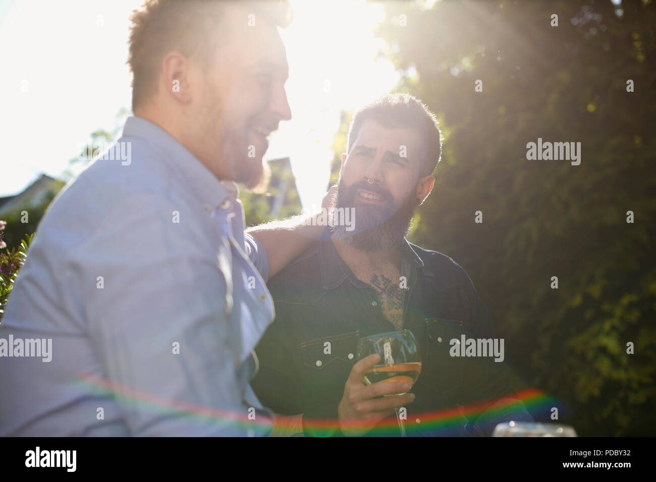 Maschio affettuoso coppia gay di bere vino in giardino soleggiato Foto Stock