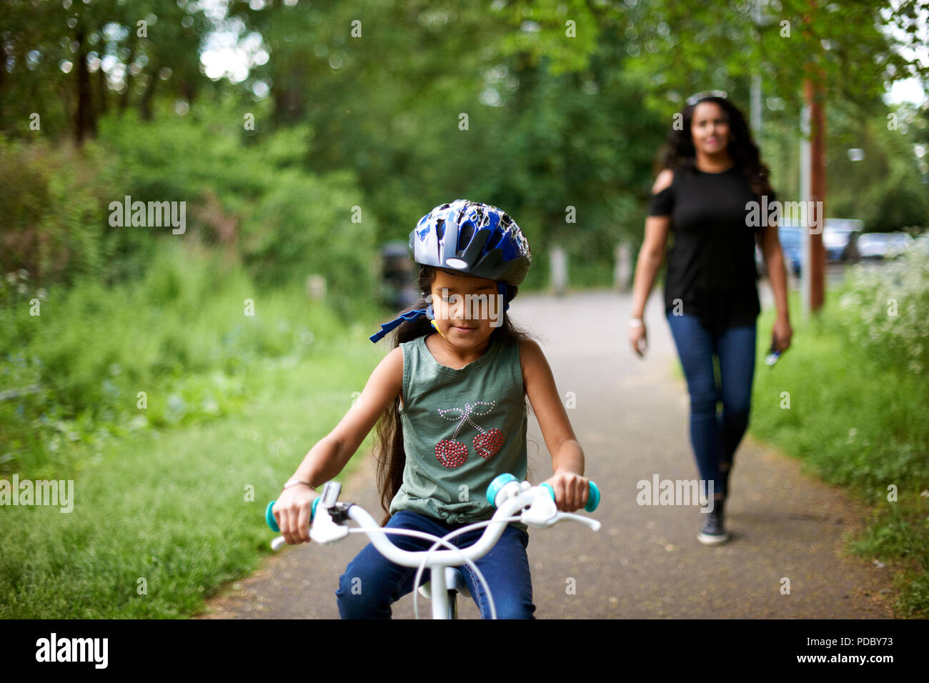 Madre guarda la figlia in bicicletta sul percorso Foto Stock