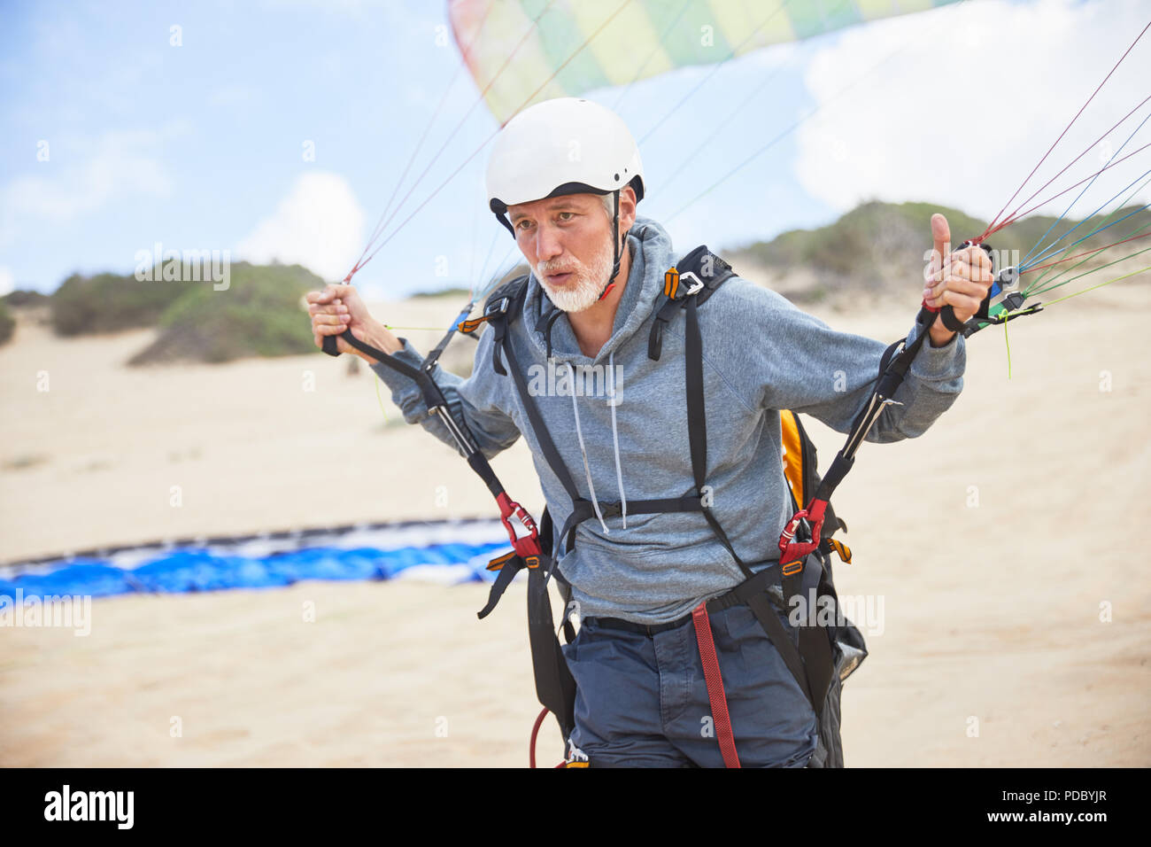 Concentrato maschio maturo di parapendio con attrezzature e paracadute sulla spiaggia Foto Stock