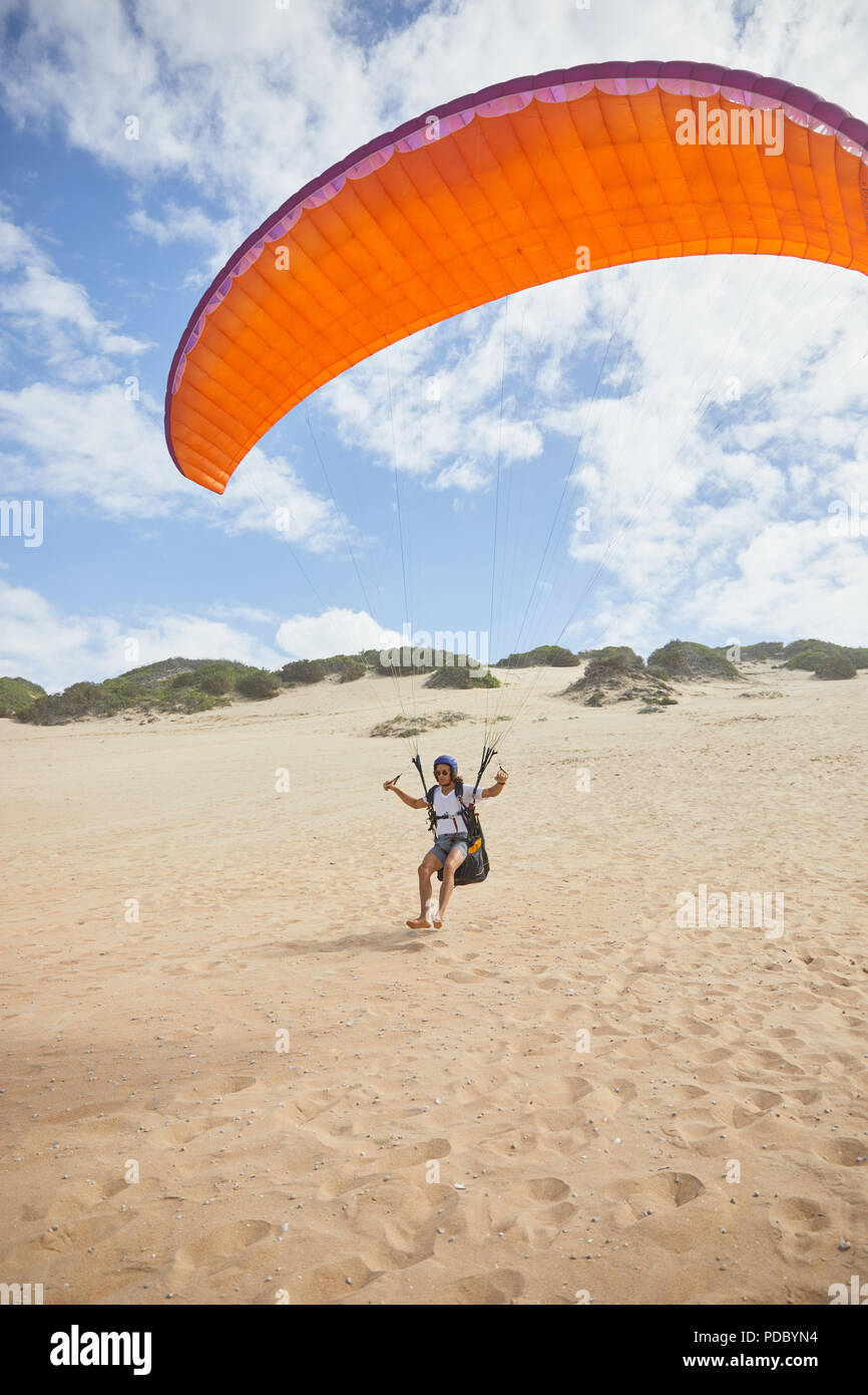 Maschio in esecuzione di parapendio con paracadute sulla spiaggia Foto Stock
