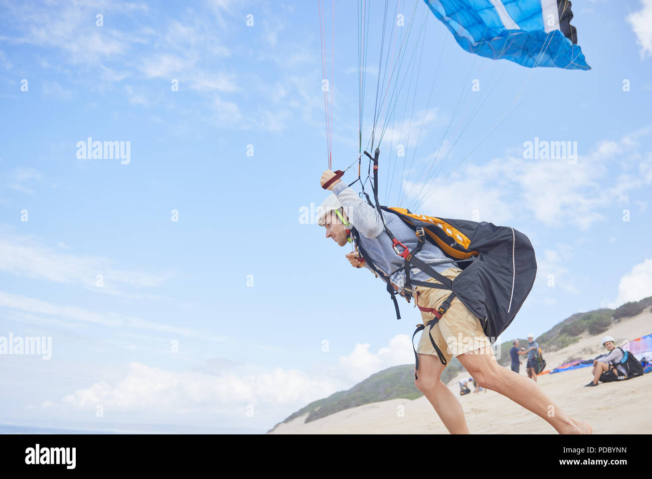 Maschio in esecuzione di parapendio con paracadute sulla spiaggia Foto Stock