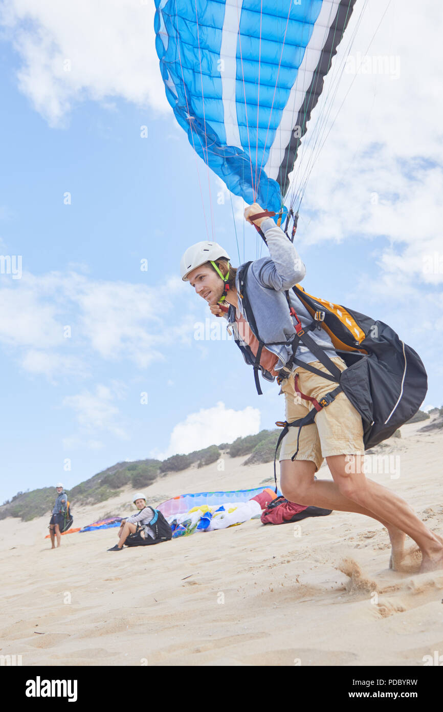 Maschio di parapendio in esecuzione sulla spiaggia Foto Stock