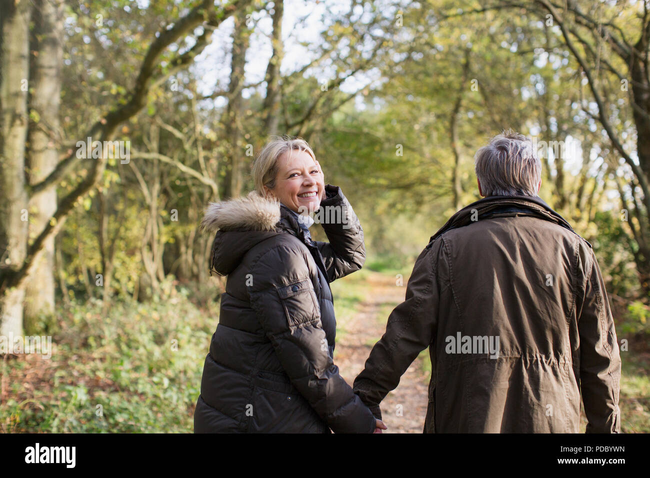 Ritratto sorridente e spensierato coppia matura Holding Hands, passeggiate nella soleggiata autunno boschi Foto Stock