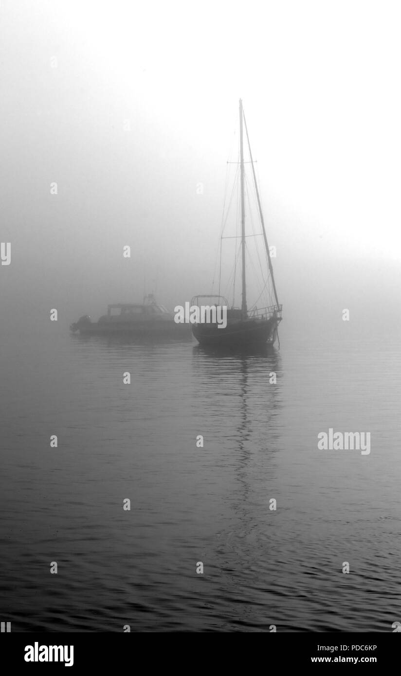 Barche di emergere dalla nebbia nelle calme acque di Walvis Bay, Namibia, in questa immagine monocromatica. Foto Stock
