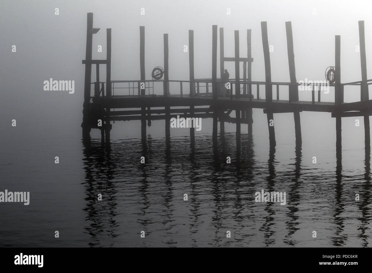 Una nebbia-coperto jetty si riflette nelle calme acque di Walvis Bay, Namibia, in questa immagine monocromatica. Foto Stock