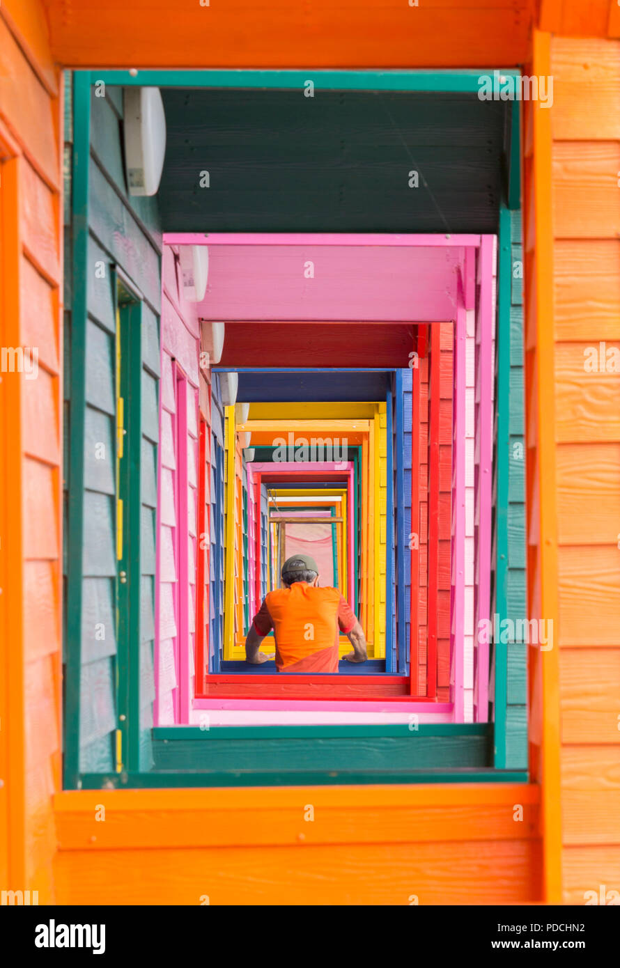 Uomo, pareggiatore maschile che si riscalda, si allunga nella porta di colorati capanne da spiaggia a Saltburn dal mare, North Yorkshire. Inghilterra. REGNO UNITO Foto Stock