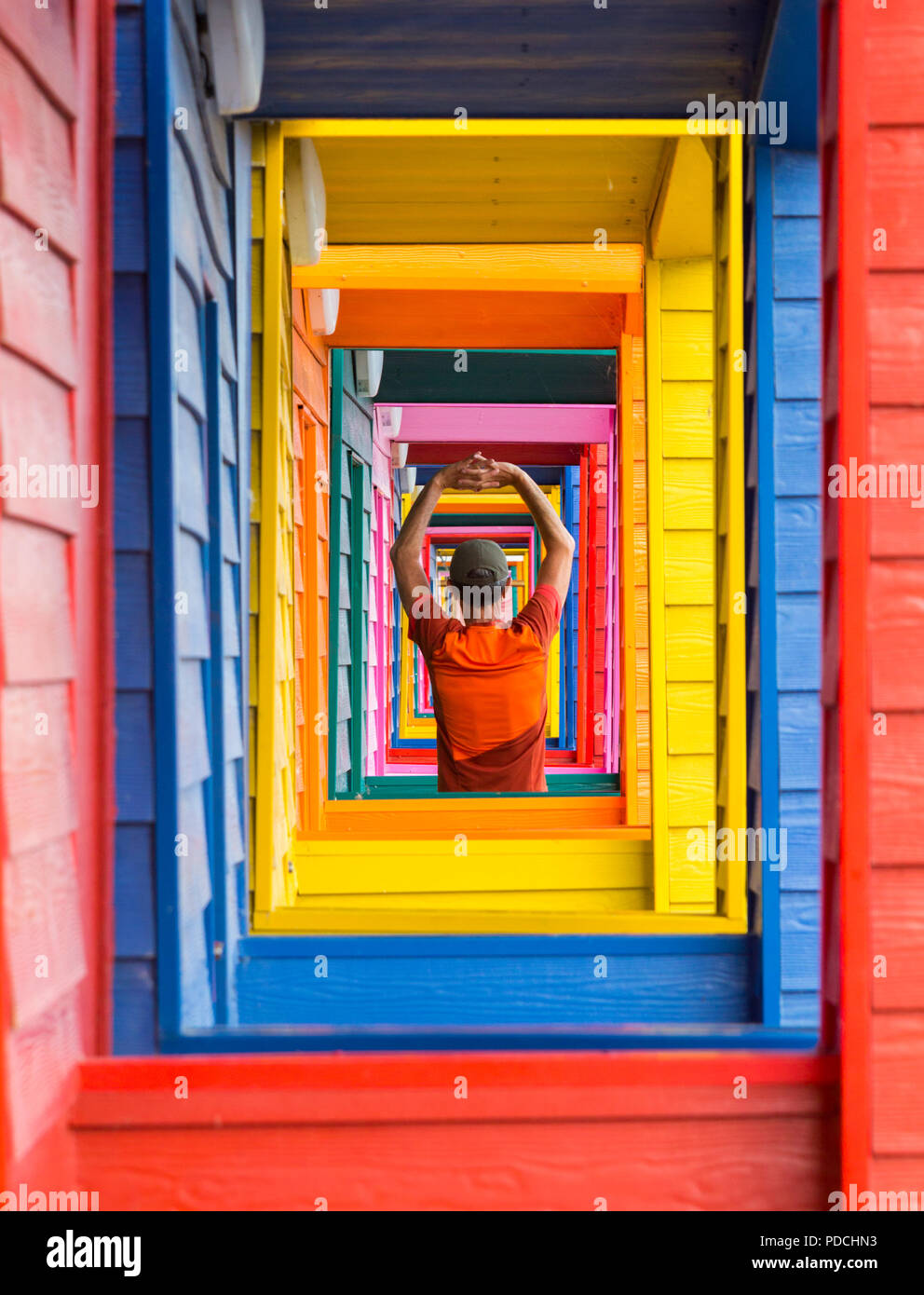Uomo, pareggiatore maschile che si riscalda, si allunga nella porta di colorati capanne da spiaggia a Saltburn dal mare, North Yorkshire. Inghilterra. REGNO UNITO Foto Stock