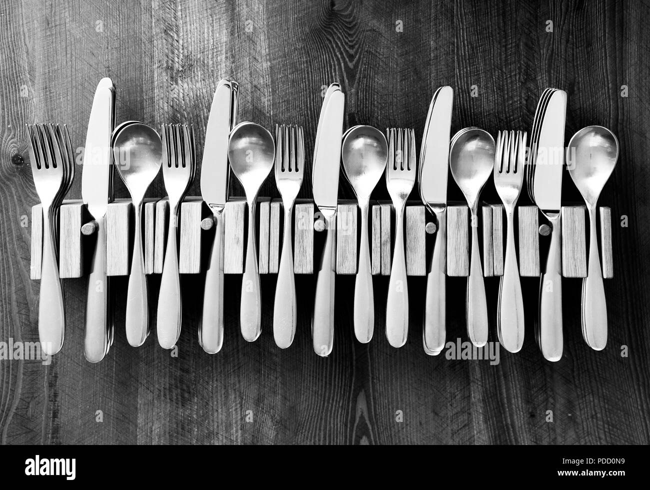 Un sacco di coltelli forchette e cucchiai fissato in una linea in cinque in legno i titolari di posate su un tavolo di legno top, fotografia in bianco e nero Foto Stock