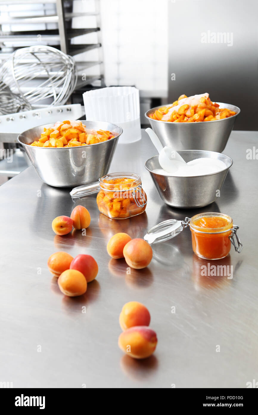 Marmellata di albicocche in un vasetto di vetro su di un acciaio inossidabile lucidato superficie in piano di pasticceria Foto Stock