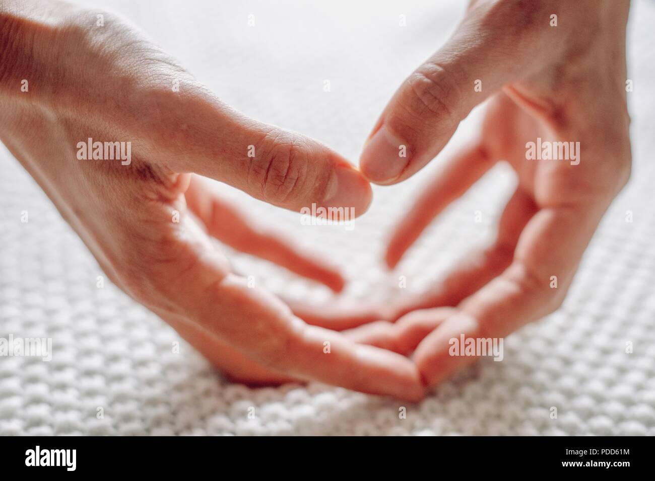 Mani femminili a forma di cuore sulla coltre bianca Foto Stock