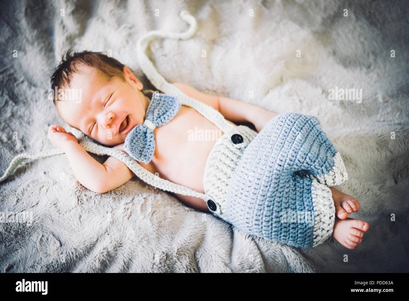 Un neonato Bambino addormentato in blu e grigio in maglia di bow tie e pantaloni Foto Stock