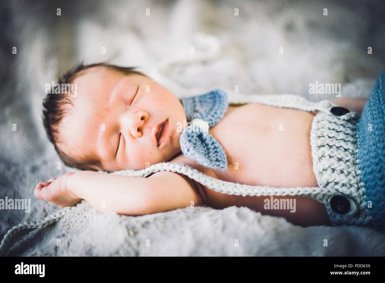 Un neonato Bambino addormentato in blu e grigio in maglia di bow tie e pantaloni Foto Stock
