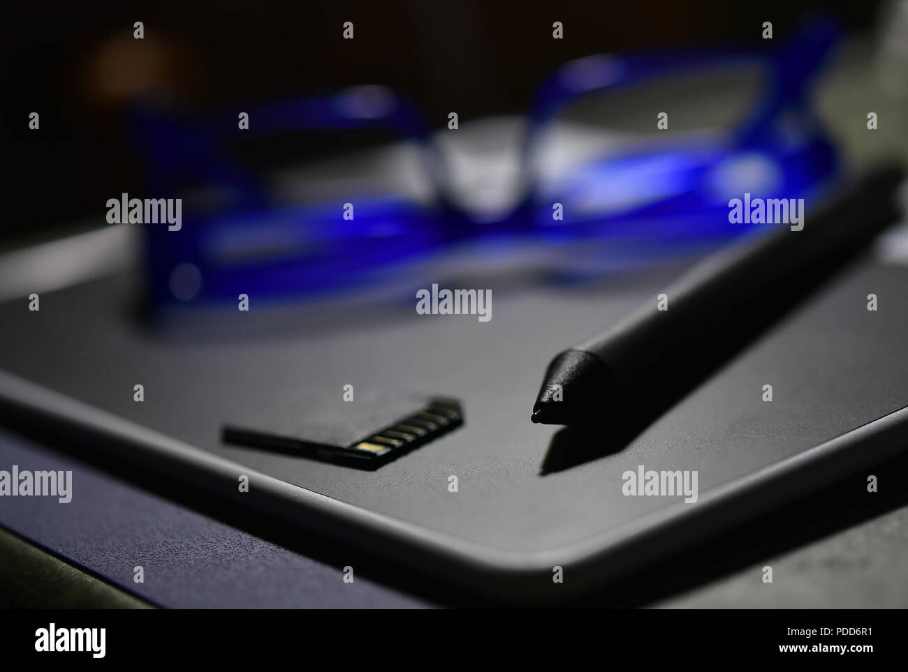 Graphic design gli strumenti Penna e compresse, blu occhiali e Memory Card sul tavolo, profondità di campo e la sfocatura dello sfondo luce bassa. Foto Stock