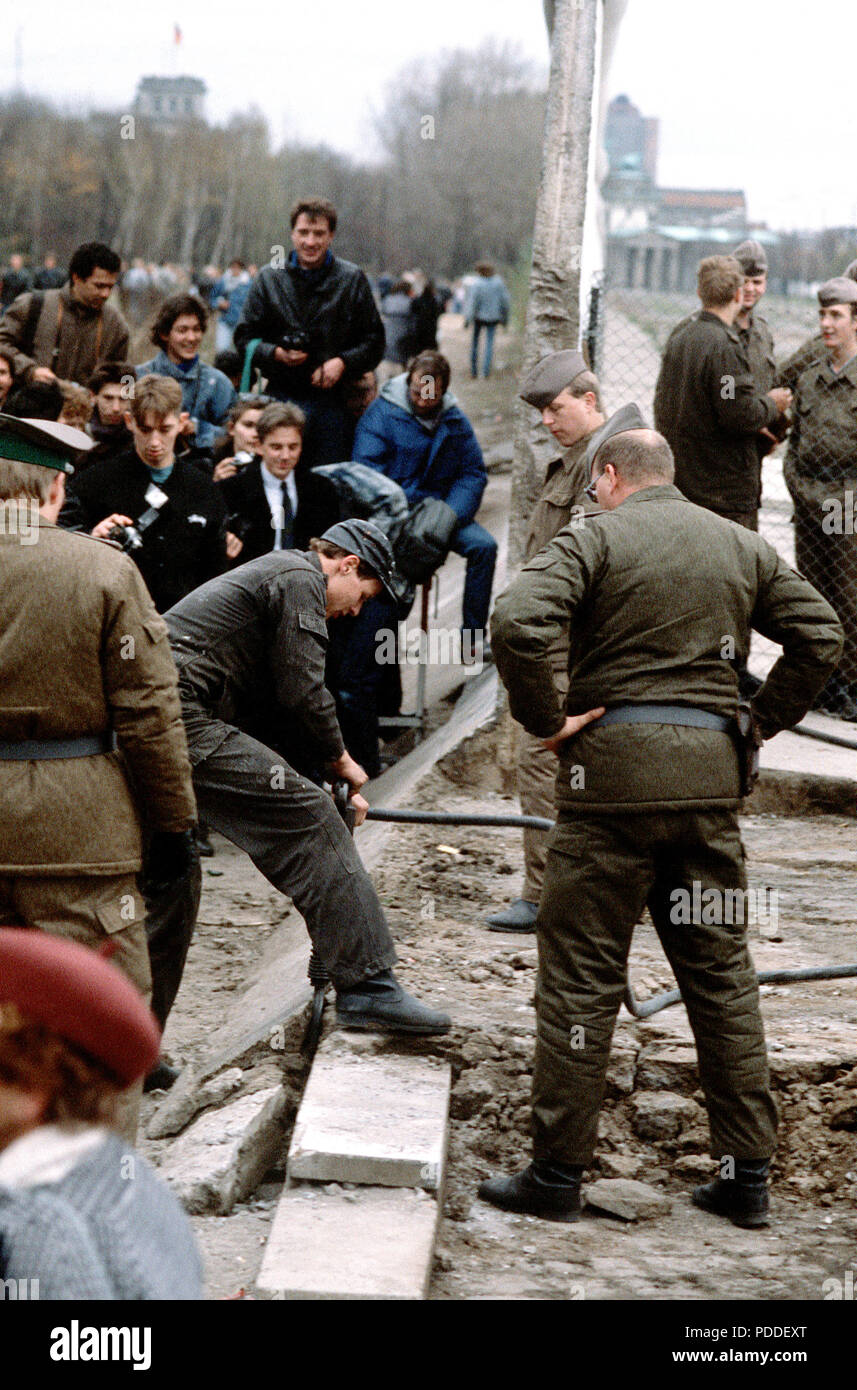 Muro di Berlino 1989 - Est della polizia tedesca e a ovest di cittadini tedeschi guardare come un operaio smantella una sezione del muro di Berlino a Potsdamer Platz. Foto Stock