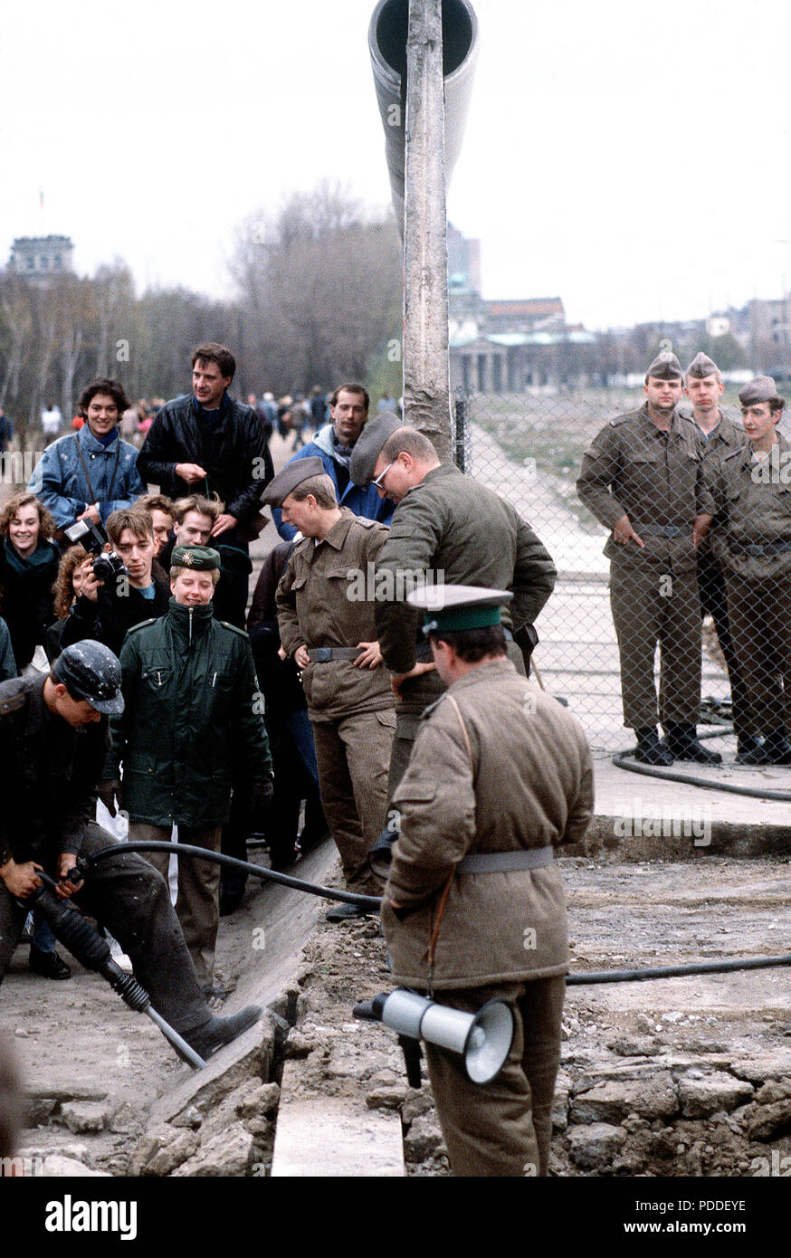 Muro di Berlino 1989 - Est della polizia tedesca e a ovest di cittadini tedeschi guardare come un operaio smantella una sezione del muro di Berlino a Potsdamer Platz. Foto Stock
