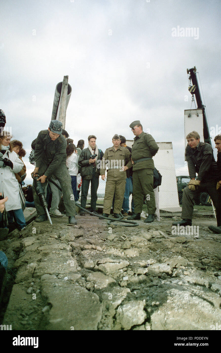 Muro di Berlino 1989 - Est della polizia tedesca e a ovest di cittadini tedeschi guardare come un operaio smantellata una sezione del muro di Berlino a Potsdamer Platz. Foto Stock