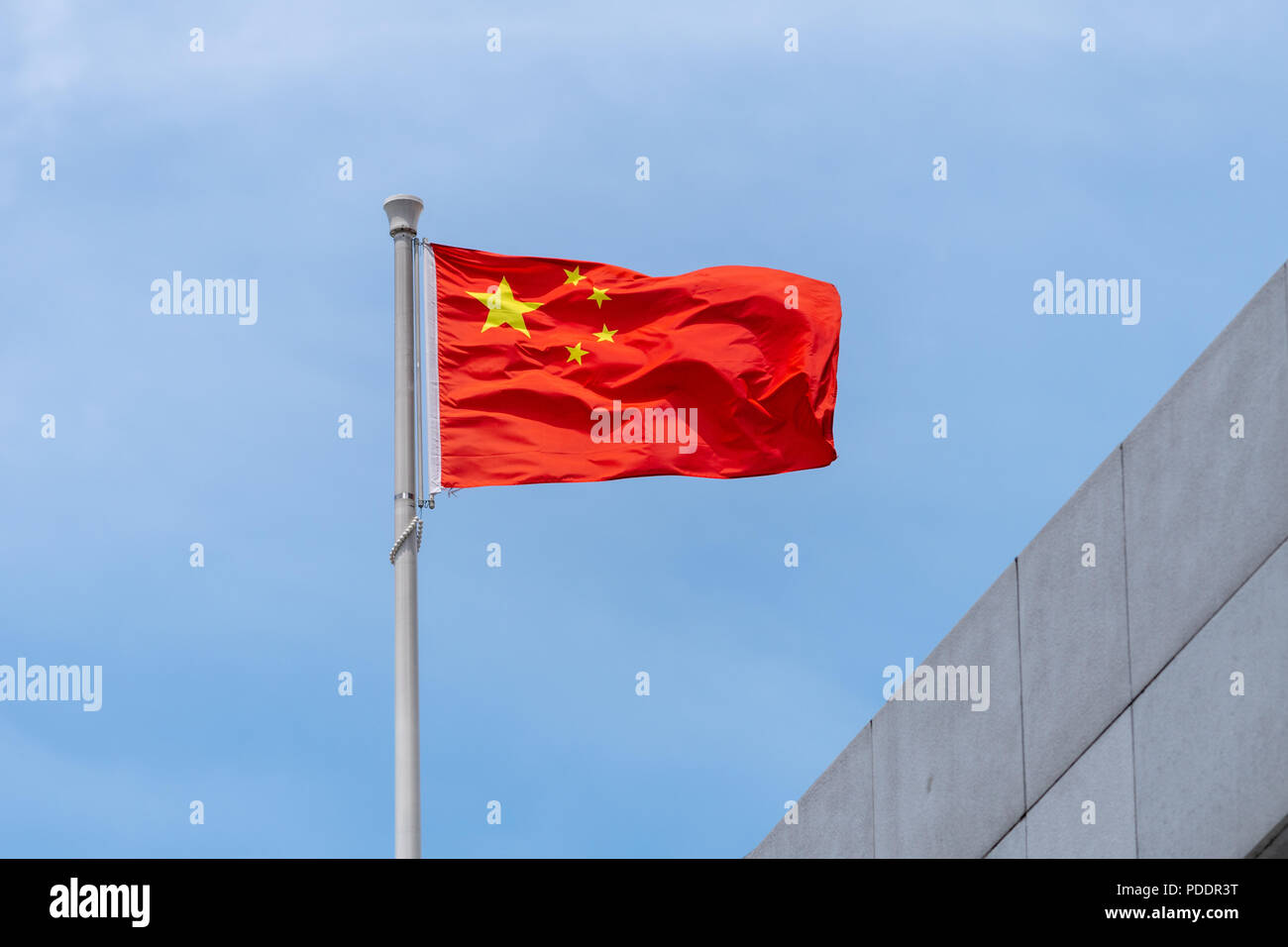 Bandiera nazionale della Repubblica popolare di Cina battenti nel vento da un palo sulla parte superiore di un edificio Foto Stock