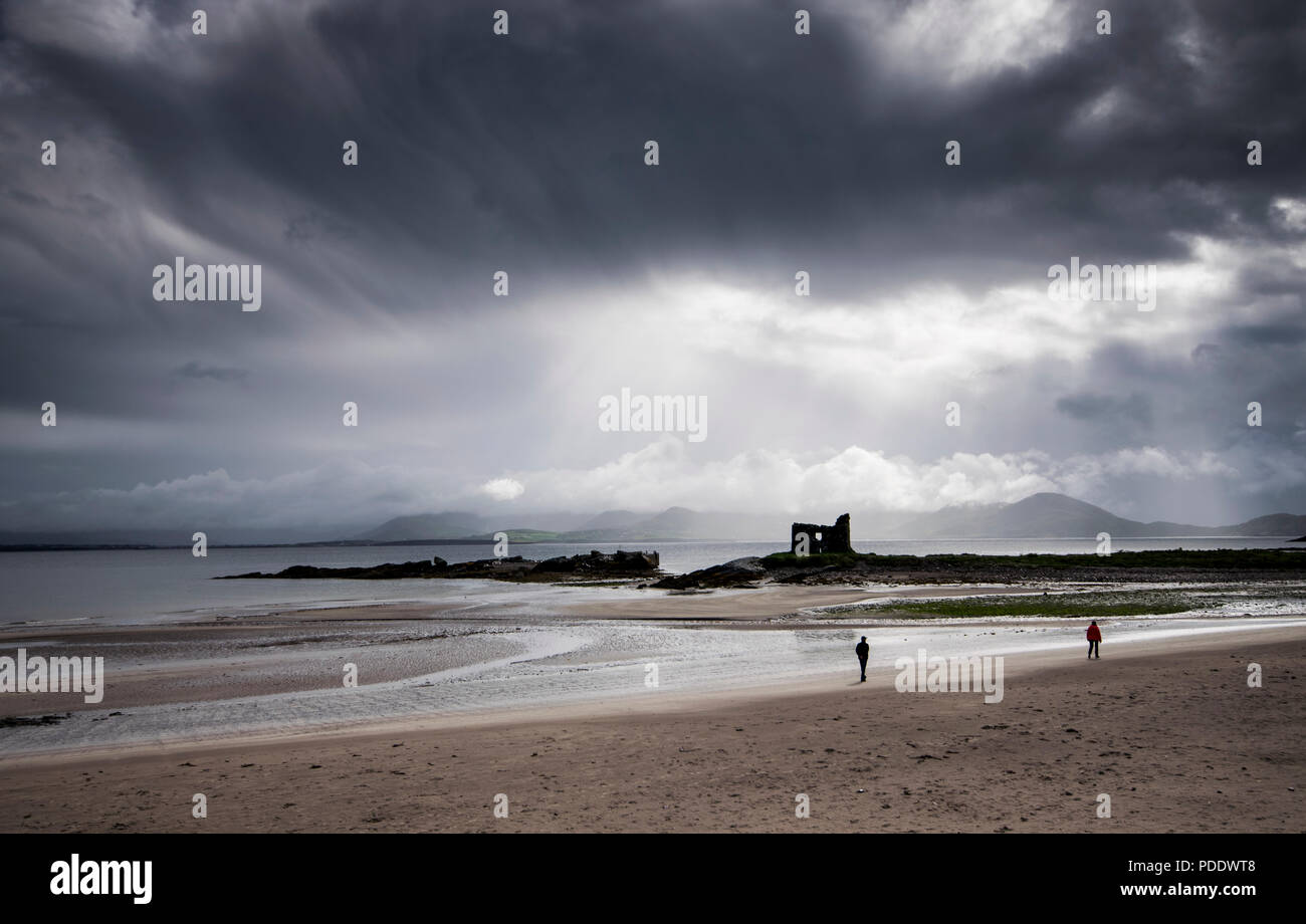 McCarthy Mór Torre a Ballinskelligs, Ring of Kerry, Irlanda, con due persone sulla spiaggia sotto un buio e meditabondo sky Foto Stock