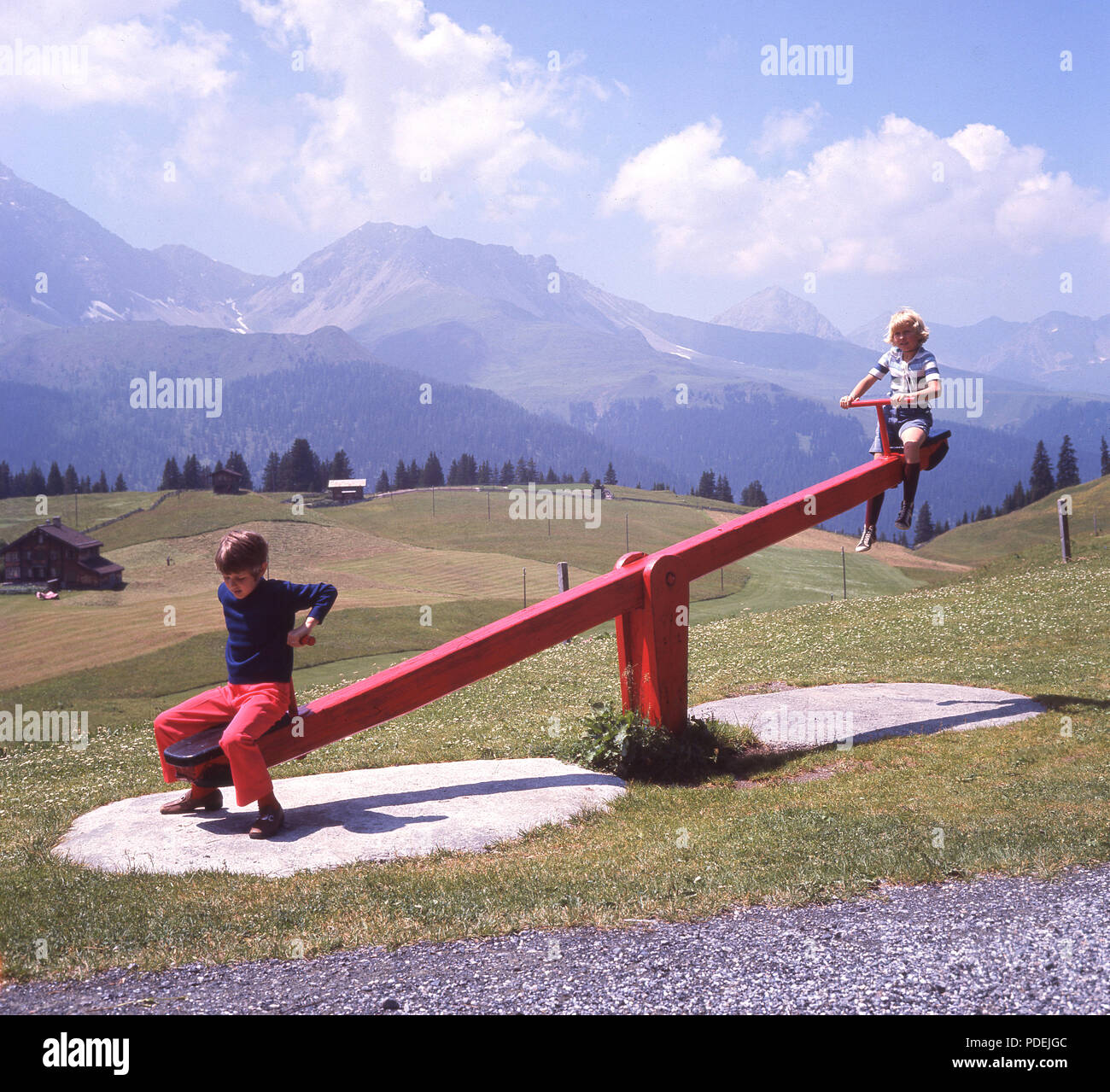 Anni sessanta, due giovani ragazzi giocare al di fuori su un dipinto luminosamente in legno tradizionali vedere-sega, situato in alta montagna delle Alpi Svizzere. Foto Stock