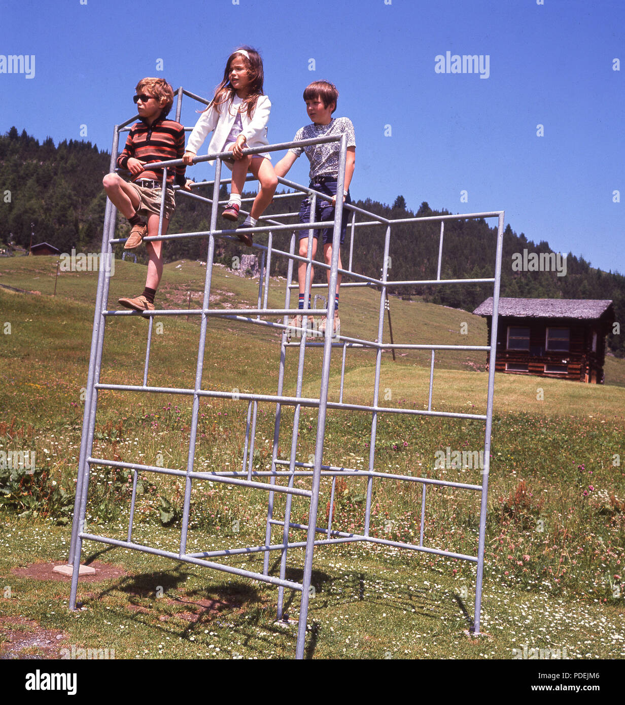 Anni sessanta, tre figli, due ragazzi e una ragazza, all'aperto all'aria fresca in piedi sulla parte superiore di un metallo del telaio di arrampicata. Foto Stock