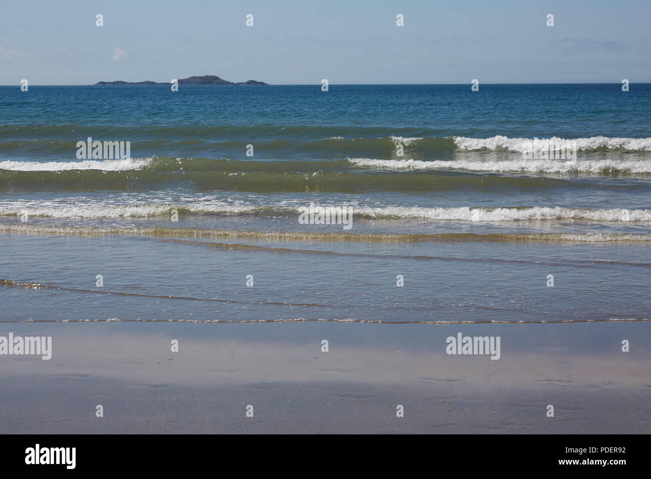 La vista del mare su una spiaggia di Gallese con dolce sciabordare di onde a riva e un'isola a distanza su una soleggiata giornata chiara Foto Stock