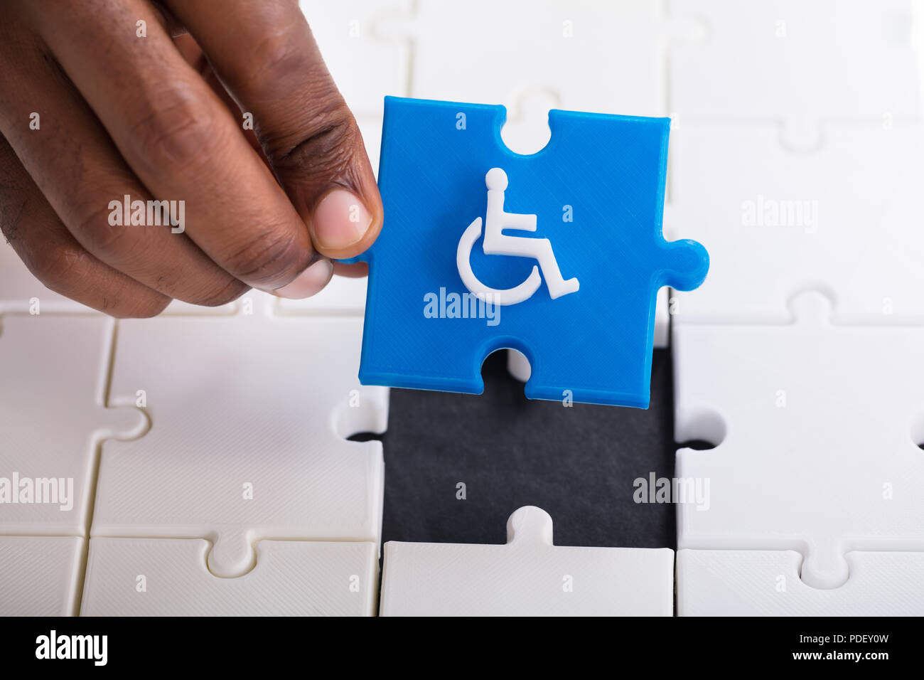 La mano di una persona in possesso di un pezzo di Blue Jigsaw Puzzle con  disabili Icona per sedia a rotelle Foto stock - Alamy