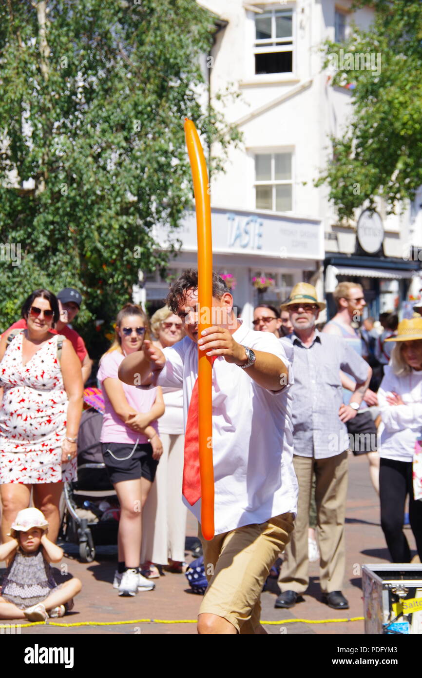 I bambini di strada di intrattenitore con Orange trucco palloncino fingendo di fuoco lungo arco. Sidmouth Folk Festival, East Devon, Regno Unito. Agosto, 2018. Foto Stock