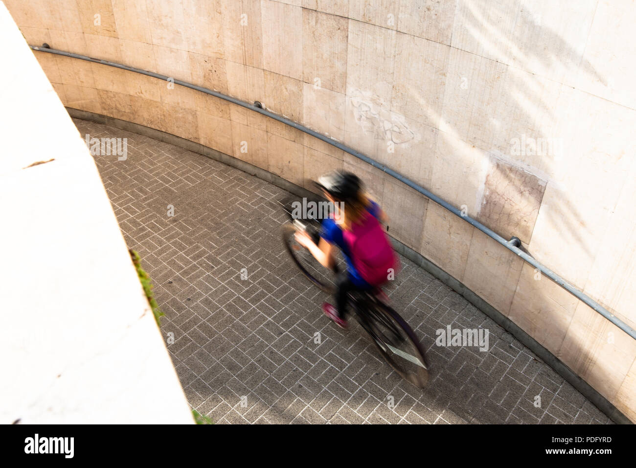Donna in bicicletta in città dalla metropolitana durante il sunshine Foto Stock